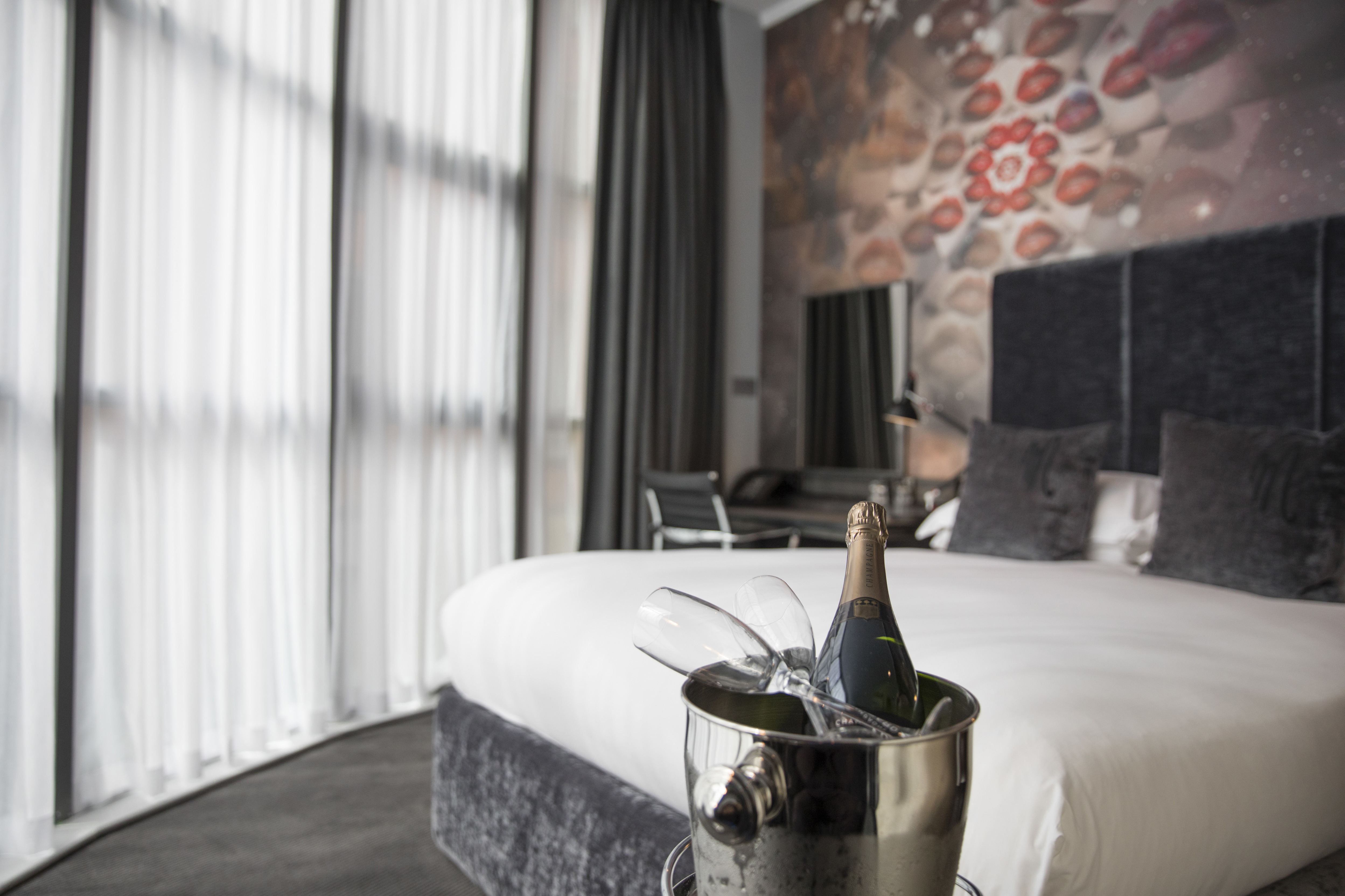 bottle of champagne with two glasses in front of a bed