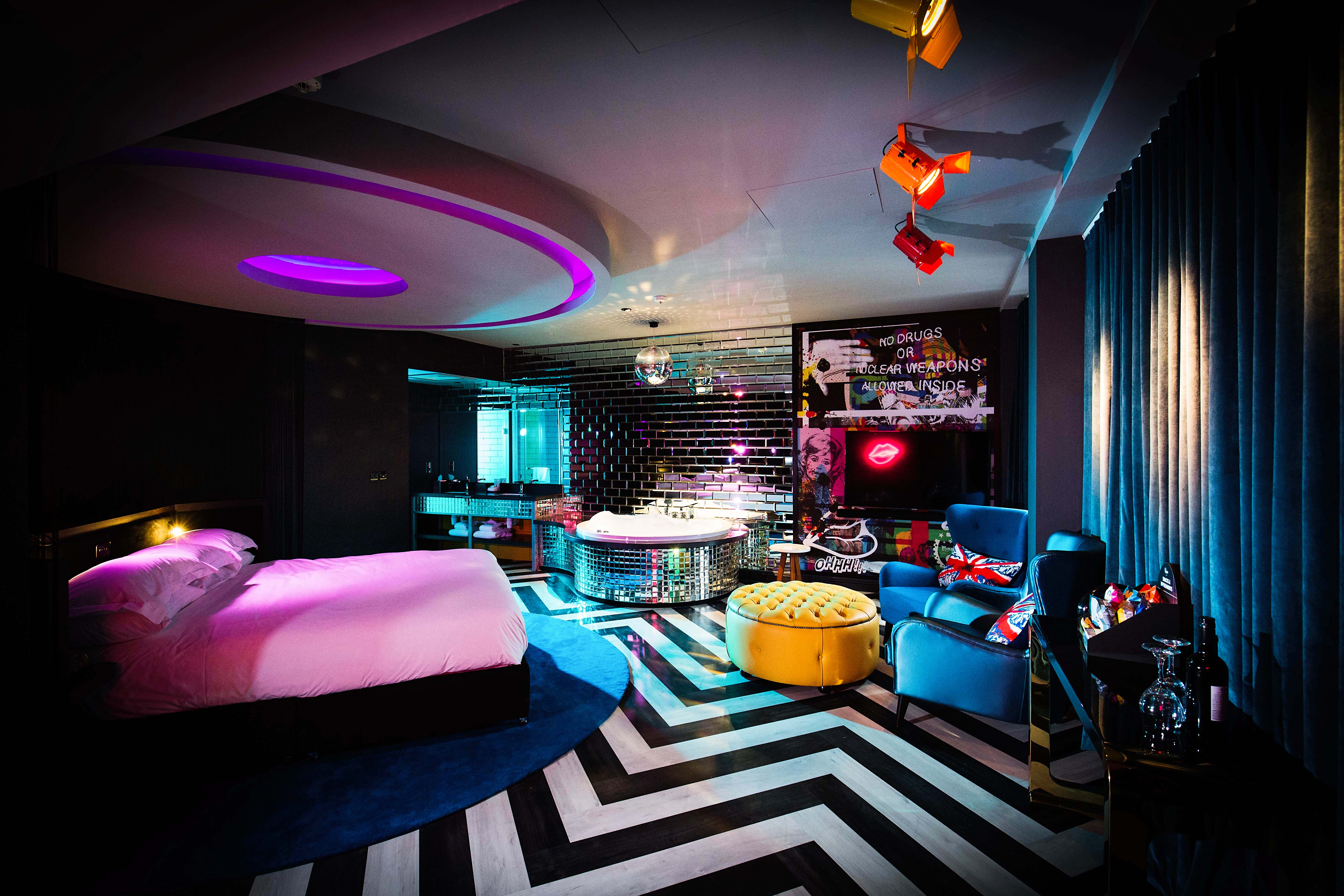 A well-furnished brightly coloured room featuring a bed, a cozy chair, and a disco ball decorated bath.