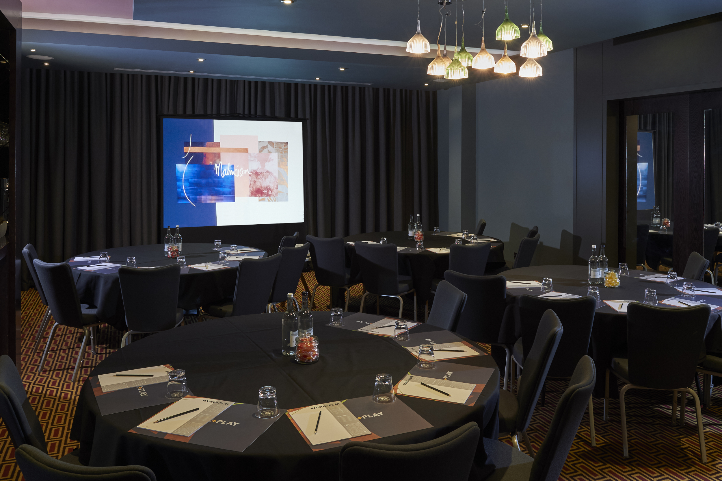 Conference room featuring tables, chairs, and a projector screen.