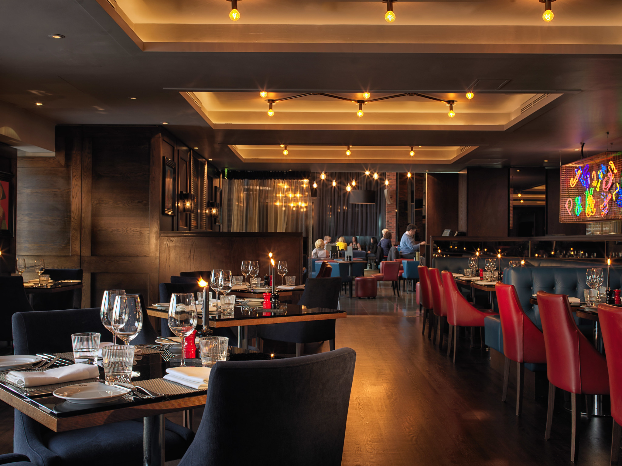 Birmingham Malmaison restaurant interior featuring grey and red seating, tables adorned with candles, glasses, and silverware.