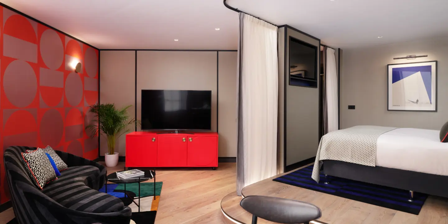 A well-furnished room featuring a comfortable bed, chair, television, and table.